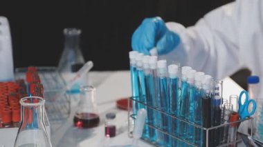 Laboratuvar bilim adamı koruyucu eldivenlerle deney tüpünü pipetle tutuyor.
