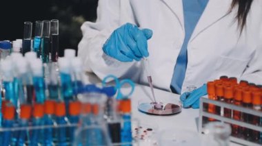 Koruyucu giysi ve palto giymiş kadın laboratuvar bilim adamı, üzerinde test tüpü olan bir tüp tutuyor..