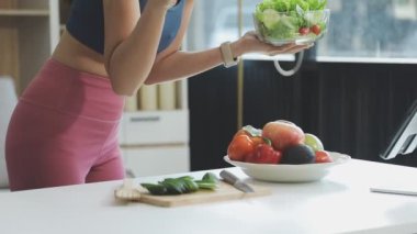 Elinde salata tutan ve mutfakta meyve suyu bardağının yanında duran genç bir kadın.