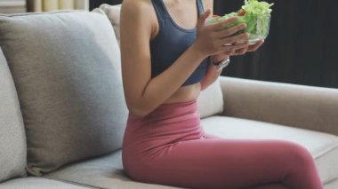 Kanepede oturan ve evinde smoothie içerken dizüstü bilgisayar kullanan genç bir kadın.