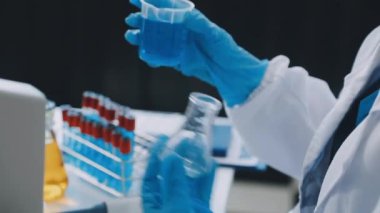 Laboratuvar asistanı laboratuarda bir deney tüpü ve kimyasal bir şişe tutuyor..