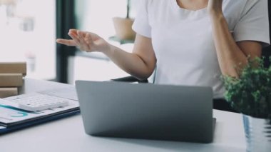 Genç Asyalı kadın dizüstü bilgisayarla çalışıyor ve ofisinde bir fincan kahve tutuyor..