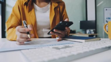 Genç Asyalı kadın modern bir ofiste deftere yazı yazıyor..