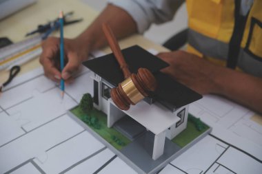 Yargıç Gavin, arka planda sarı bir kaskla bina planları hazırlıyor. İnşaat ve mühendislikle ilgili konularla ilgili yasalar. İnşaat hukuku kavramı.