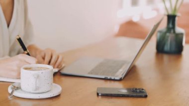 Kadın elleri bir defter tutuyor, evden çalışıyor.