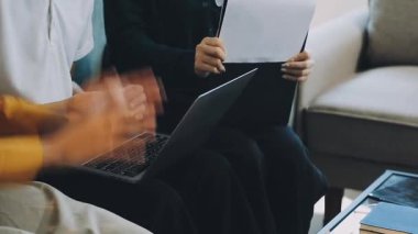 Beyaz gömlekli ve siyah pantolonlu genç adam oturuyor ve elinde bir dizüstü bilgisayar tutuyor.