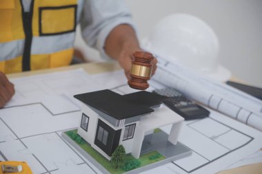Yargıç Gavin, arka planda sarı bir kaskla bina planları hazırlıyor. İnşaat ve mühendislikle ilgili konularla ilgili yasalar. İnşaat hukuku kavramı.