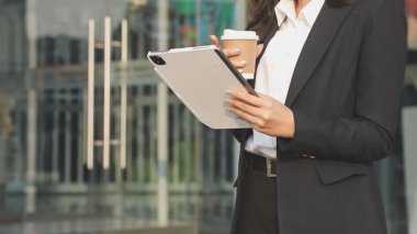Elinde tablet tutan genç bir kadın modern binanın arka planında duruyor.
