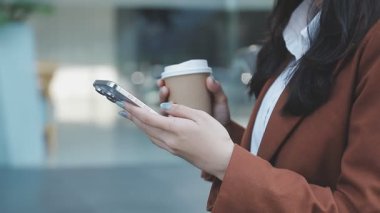 Genç bir kadın elinde kahve fincanı tutarken akıllı telefon kullanıyor.