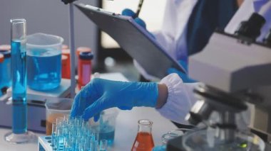 Mikroskop tutan ve test tüplerine bakan bir bilim adamı.