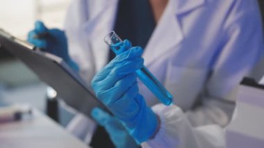 Beyaz önlüklü laboratuvar asistanı elinde bir şişe tutuyor.