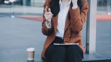 Takım elbiseli iş kadını akıllı telefon kullanıyor ve şehirde kahve içiyor.