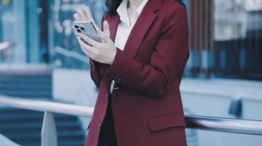 Asyalı iş kadını şehir caddesinde cep telefonu kullanıyor..