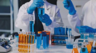 Koruyucu takım elbiseli bir laboratuar asistanı test tüplü gözlükler ve cam tüpte kimyasal bir sıvı..