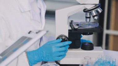 Mavi ceketli ve eldivenli bir laboratuar bilim adamı elinde bir pipet tutuyor.