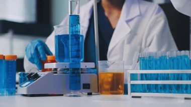 Mavi laboratuvar önlüklü laboratuvar çalışanının test tüpünü tutup sıvı test tüpüne baktığı yer..
