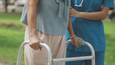 Genç bir kadın parkta yürüyor, elini kullanarak yürüyor. Tekerlekli sandalyeli yaşlı kadın ve kadın