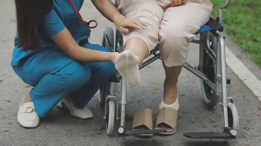 Tekerlekli sandalyedeki Asyalı hemşire bacağı olan hastayı tutuyor.