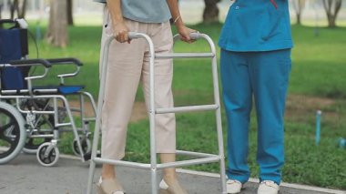 Genç hemşire parkta bastonuyla yürüyen kadına yardım ediyor.