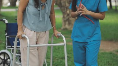 Hemşire tekerlekli sandalyeli hastaya parkta yürümesi için yardım ediyor..