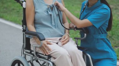 Genç bayan hemşire ve hasta parkta tekerlekli sandalyede yürüyorlar.