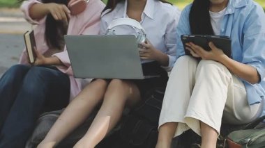 Genç Asyalı kadın tablet bilgisayar kullanıyor ve parktaki çimlerde oturuyor.