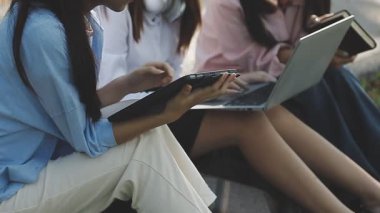 Dizüstü bilgisayar kullanan iki genç iş kadını bankta oturuyor.