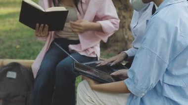 Genç Asyalı kadın parkta otururken dizüstü bilgisayar kullanıyor.