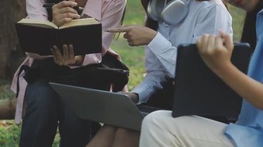 Genç insanlar çimenlerde dizüstü bilgisayarlarıyla oturup konuşuyorlar..