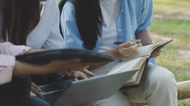 Genç Asyalı kadınlar parkta dizüstü bilgisayar ve defterle ders çalışıyorlar..