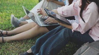 Genç Asyalı kadınlar parkta oturup dizüstü bilgisayar kullanıyorlar.