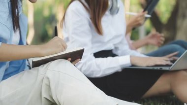 Genç bir kadın dizüstü bilgisayar kullanıyor ve parktaki deftere yazı yazıyor. işletme ve eğitim kavramı.