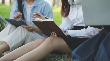 Genç Asyalı kadın öğrenciler çimenlerde oturur ve parkta kitap okurlar.