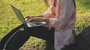 Kız çimenlerde oturuyor ve laptopunu kullanıyor.