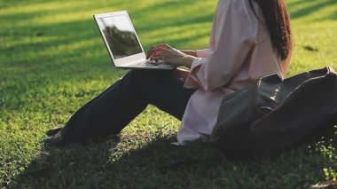 Bilgisayarlı genç bir kadın parkta bankta oturuyor.