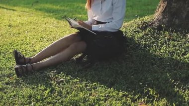 Beyaz elbiseli kadın çimlerin üzerinde oturuyor ve kitap okuyor.