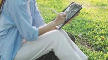 Genç kız yeşil çimlerin üzerinde dijital tablet kullanıyor.