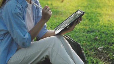 Parkta kitap ve tabletle Asyalı genç bir öğrenci.