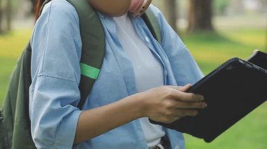 Tablet tutan ve parkta akıllı telefon kullanan bir kadın.