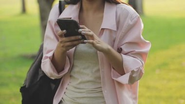 Gün batımında parkta akıllı telefon kullanan genç bir kadın..