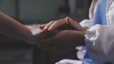Doktor hastayla el ele tutuşuyor.