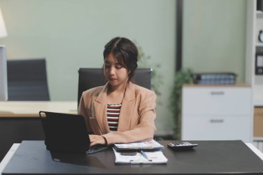 Telework konsepti - Asyalı iş kadını video toplantısına katılmak için dizüstü bilgisayar kullanır ve evdeki dijital tabletine notlar yazar