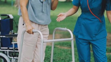 Hemşire yaşlı kadına yürüyen hasta için yardım ediyor.
