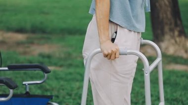 Tekerlekli sandalyedeki genç bir kadın parkta boş bir tekerlekli sandalyede duruyor. Bir adam parkta bir yürüyüşçüyle yürüyor..