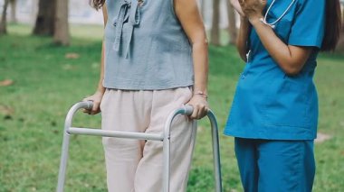 Hemşire ve hastası ile birlikte parkta yürüyen Asyalı kadın.