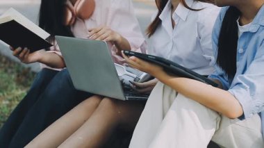 Genç bir kadın parkta dizüstü bilgisayarla oturup ders çalışıyor..