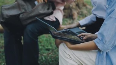 Genç bir kadın parkta otururken dizüstü bilgisayar kullanıyor.