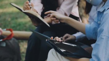 Genç Asyalı bir adam doğada arkadaşlarıyla kitap okuyor..