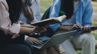 Genç Asyalı öğrenciler parkta bankta oturuyorlar ve tablet kullanıyorlar..