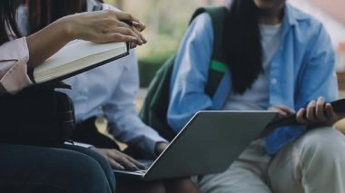 Genç Asyalı öğrenciler kampüste dizüstü bilgisayar ve kitaplarla çalışıyorlar..